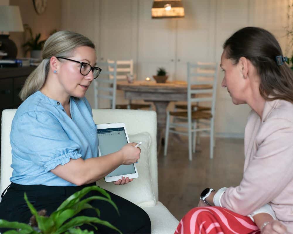 Hypnotherapist Joanna Kudzielka explaining the initial consultation process to a client using an iPad in a calm, professional setting